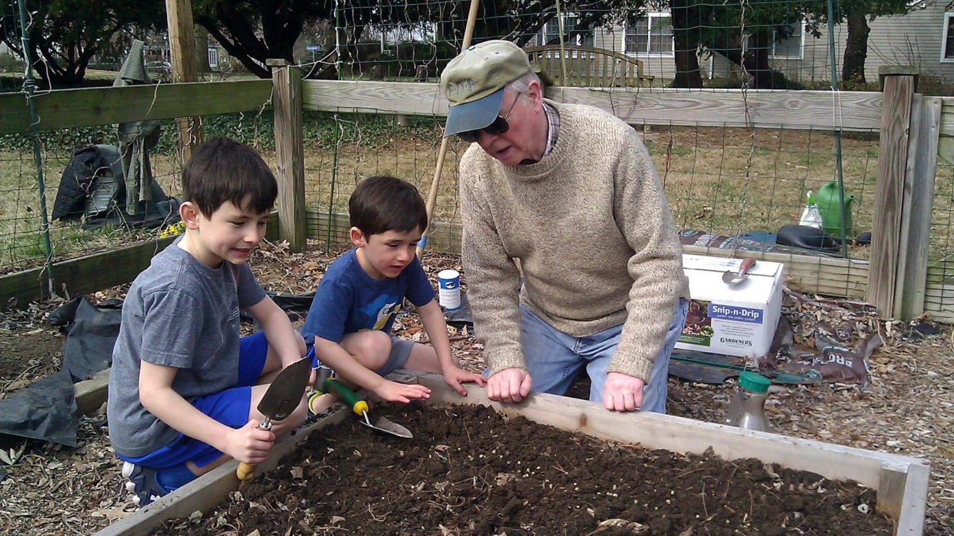 older man and two young boys working together in a garden