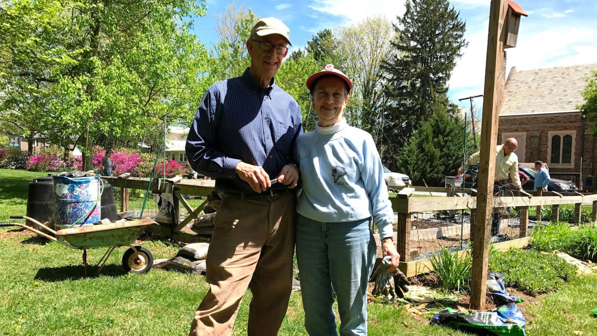 Older man and woman smiling in front of a garden that is being made