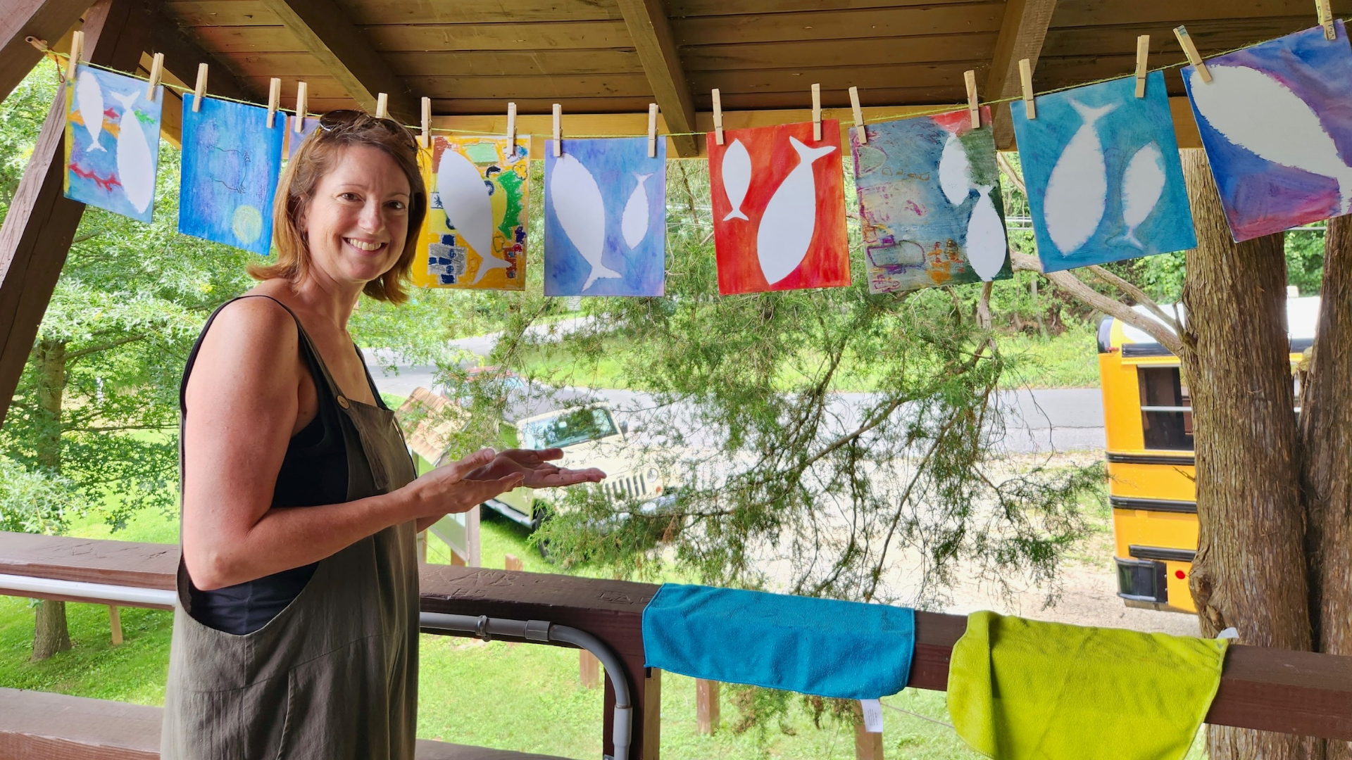 Woman smiling in front of laundry line with children's paintings of fish at camp beetree.